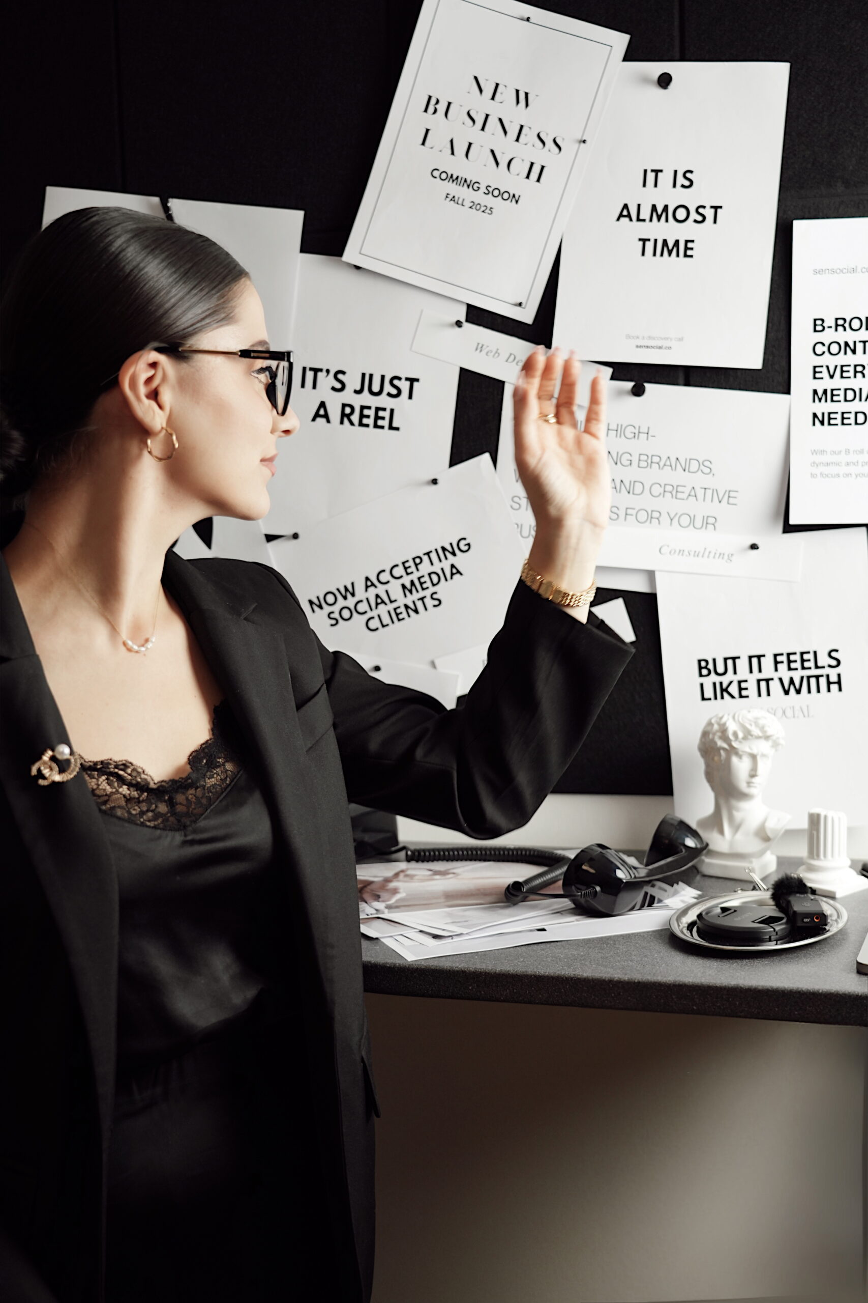 Professional woman in a black suit working in a modern creative office surrounded by marketing visuals, representing a Vienna-based digital marketing and branding agency.