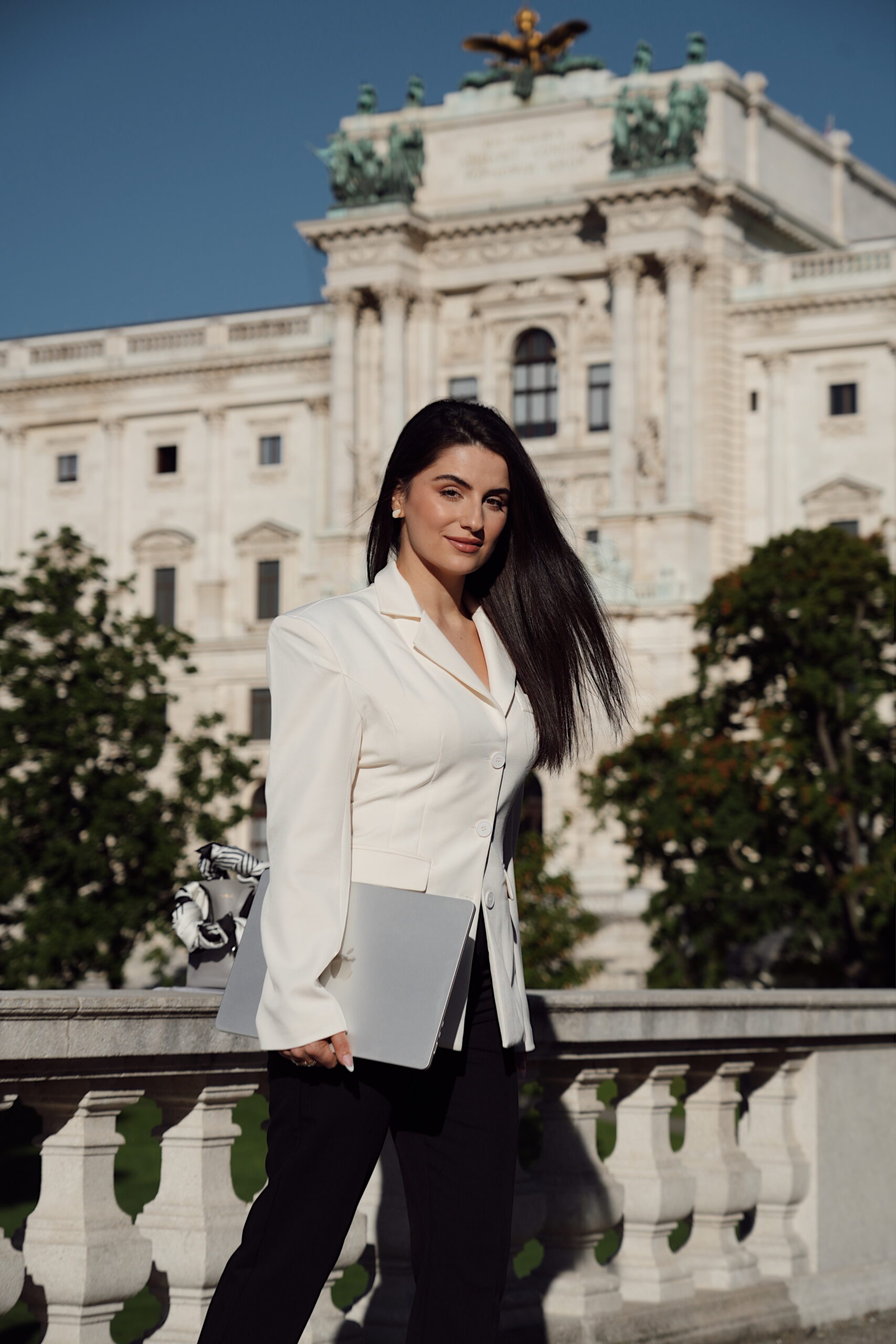 Professional woman in a white blazer holding a laptop in front of a historic Vienna building, symbolizing modern brand strategy and digital marketing expertise.